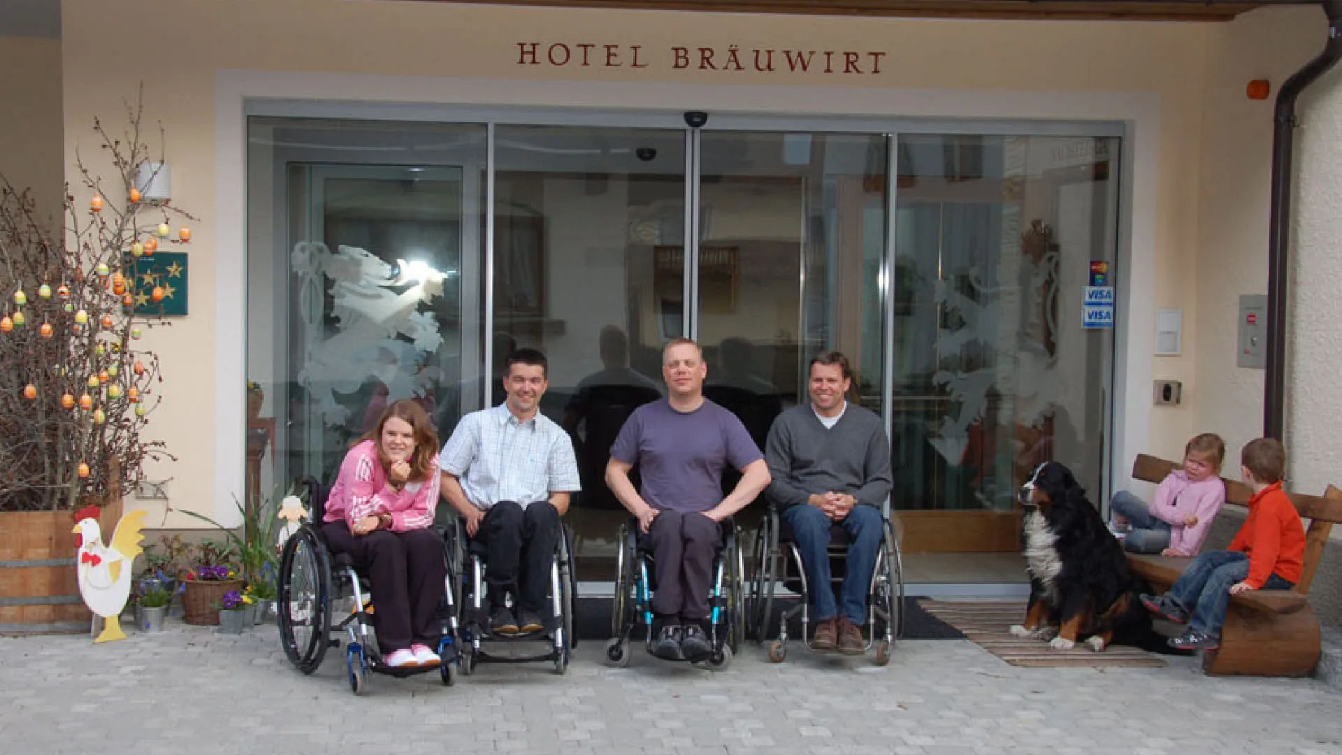 Vier Personen in Rollstühlen vor dem Hotel Brauwirt